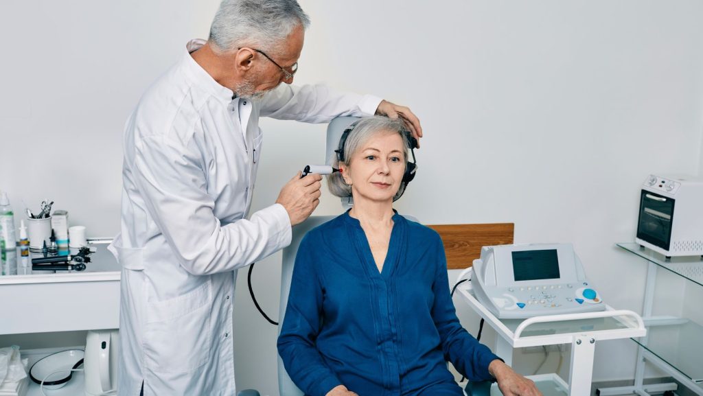 A doctor standing beside a patient conducting a hearing test.