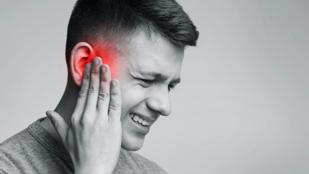 A man holding his ear, showing signs of Tinnitus pain