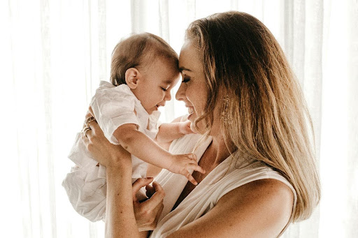 Mother and baby smiling at each other, foreheads touching, in soft natural light. 